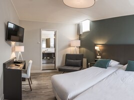 Habitación de hotel moderna con una cama grande, un escritorio con silla, televisión y baño visible a través de una puerta abierta.