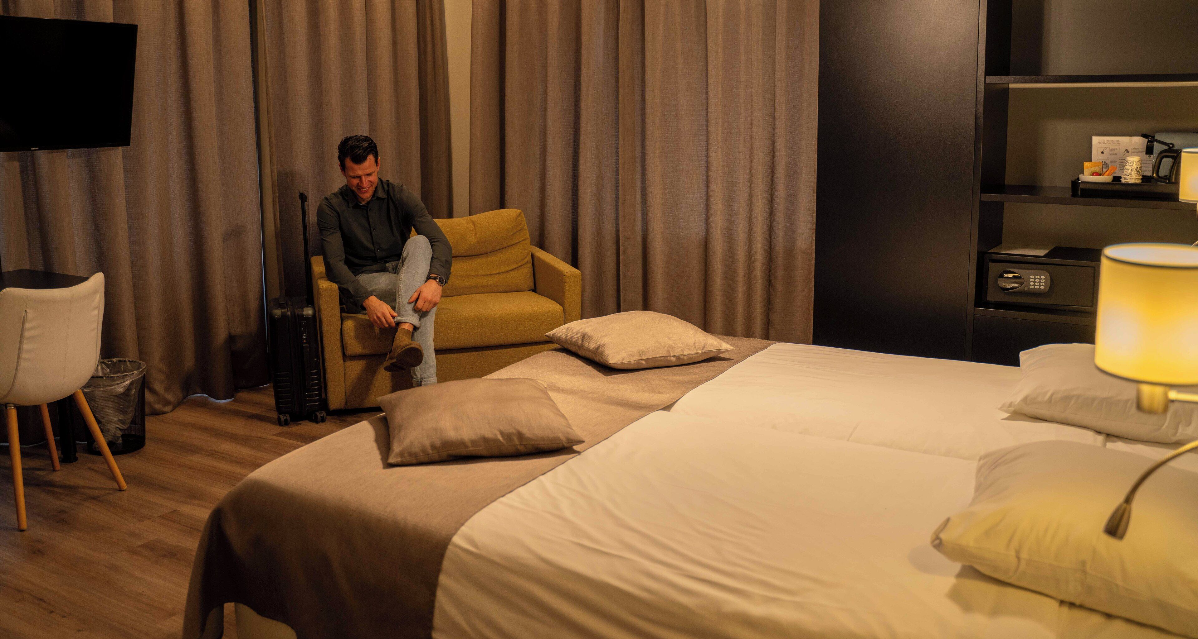 A hotel room with a bed, a chair, a TV, and a desk with a lamp.