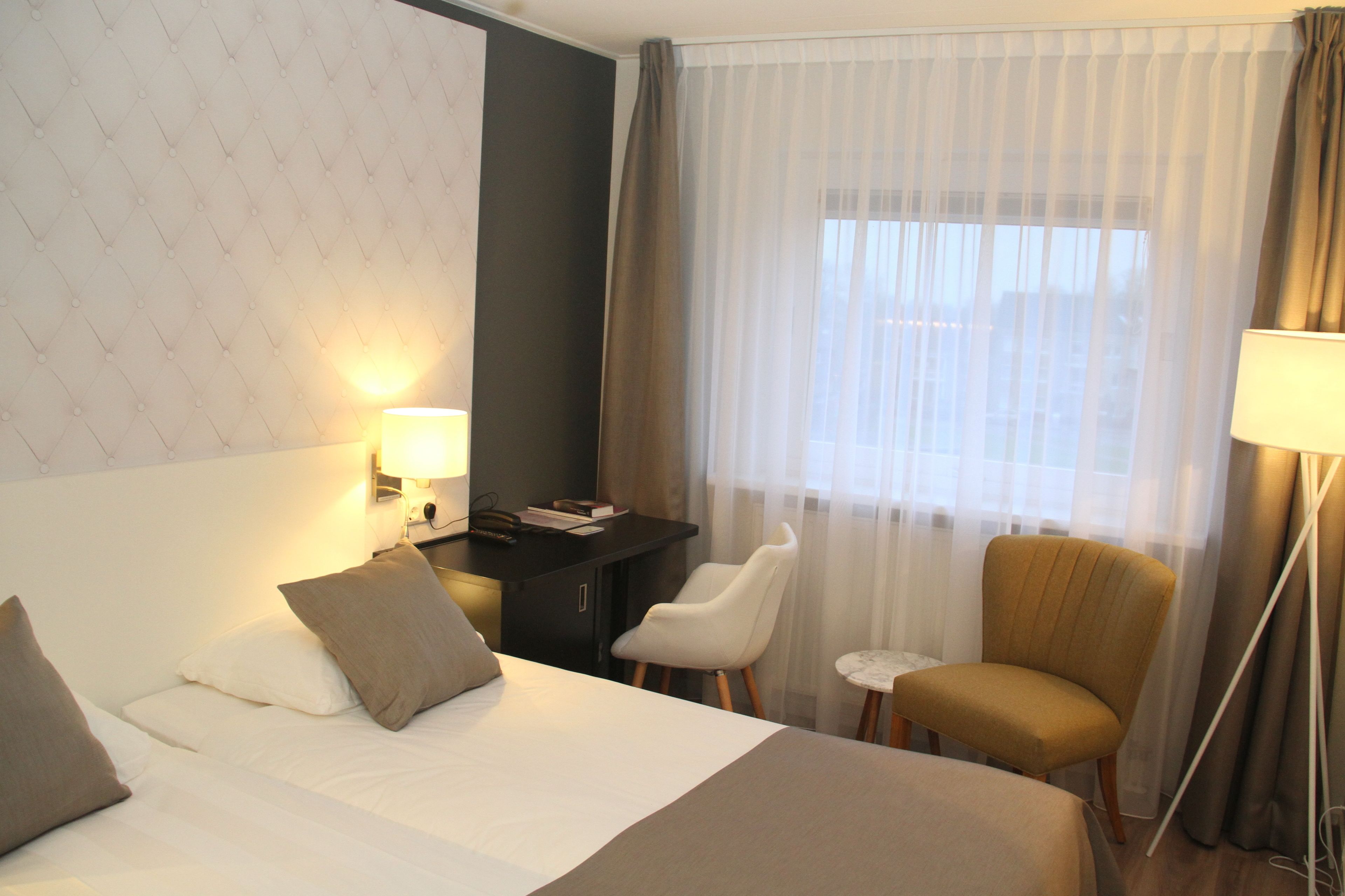 Una habitación de hotel con cama, escritorio, silla y lámpara.