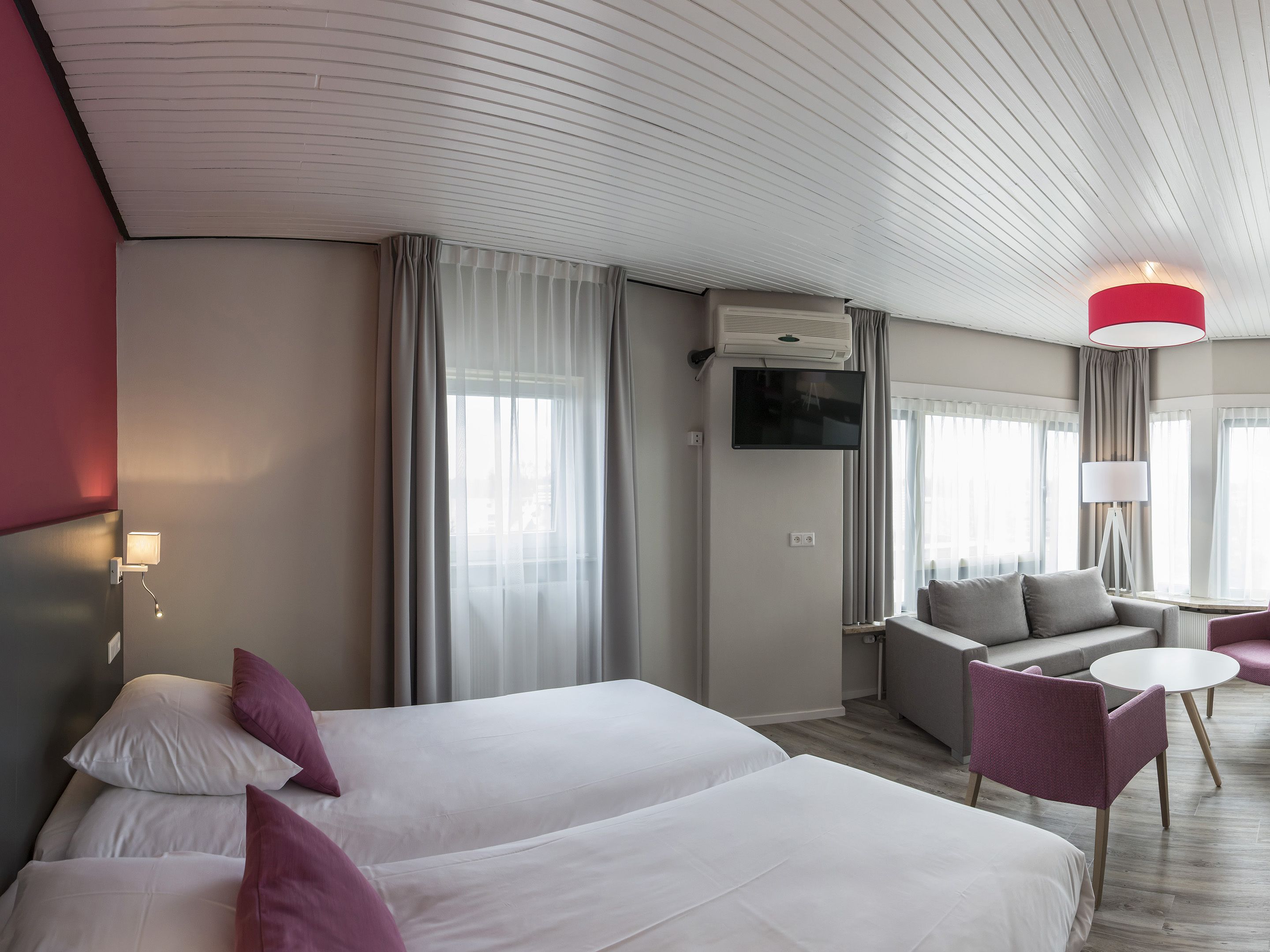 Una habitación de hotel con dos camas, un televisor, una lámpara roja y una mesita.