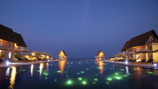 A pool with thatched-roof structures on either side, reflecting lights on the water. - Maalu Maalu Resort & Spa (Pasikuda)