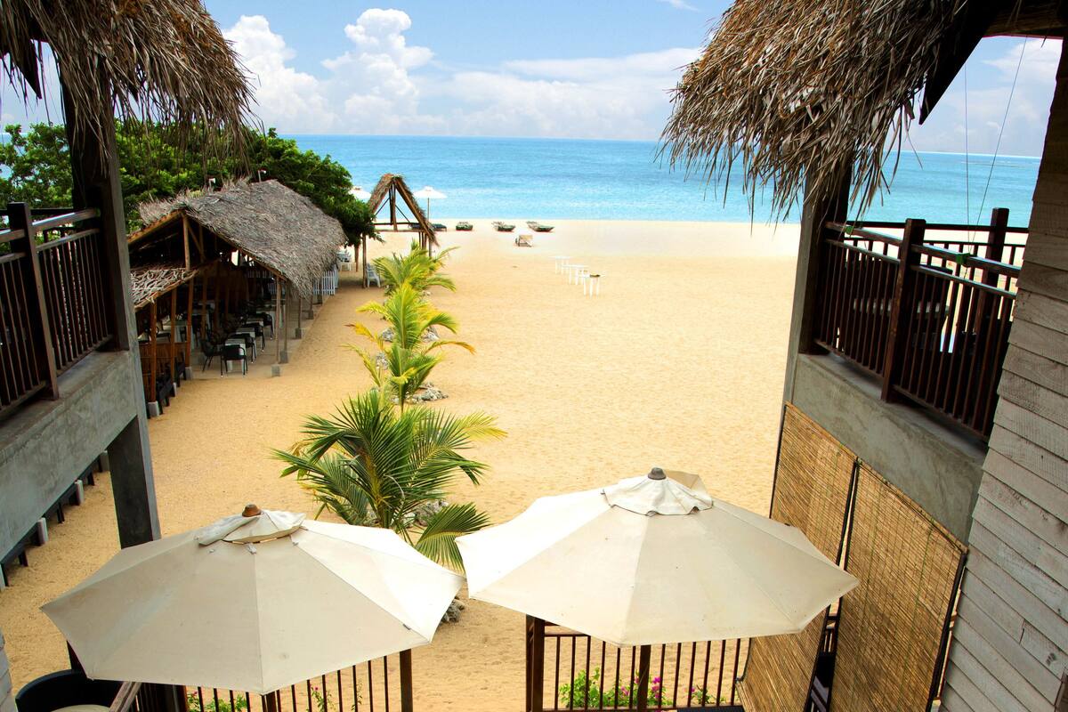 Zona de piscina con vistas a la playa, con sillones de descanso y sombrillas.