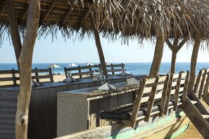 Una terraza de madera con mesas y sillas, con vista a una playa y al mar.