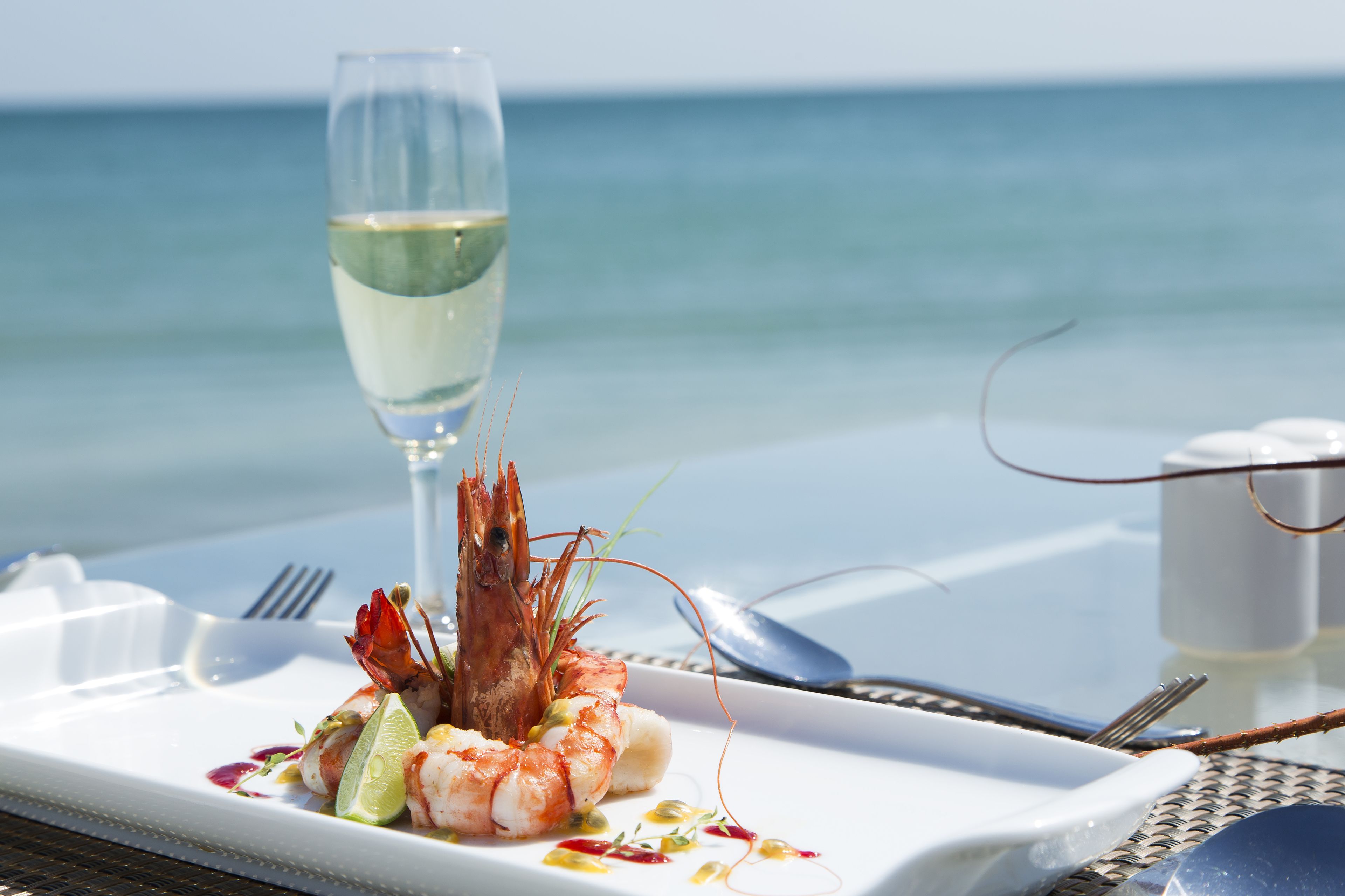 Ein Fischgericht mit einem Glas Weißwein auf einem Tisch am Meer.