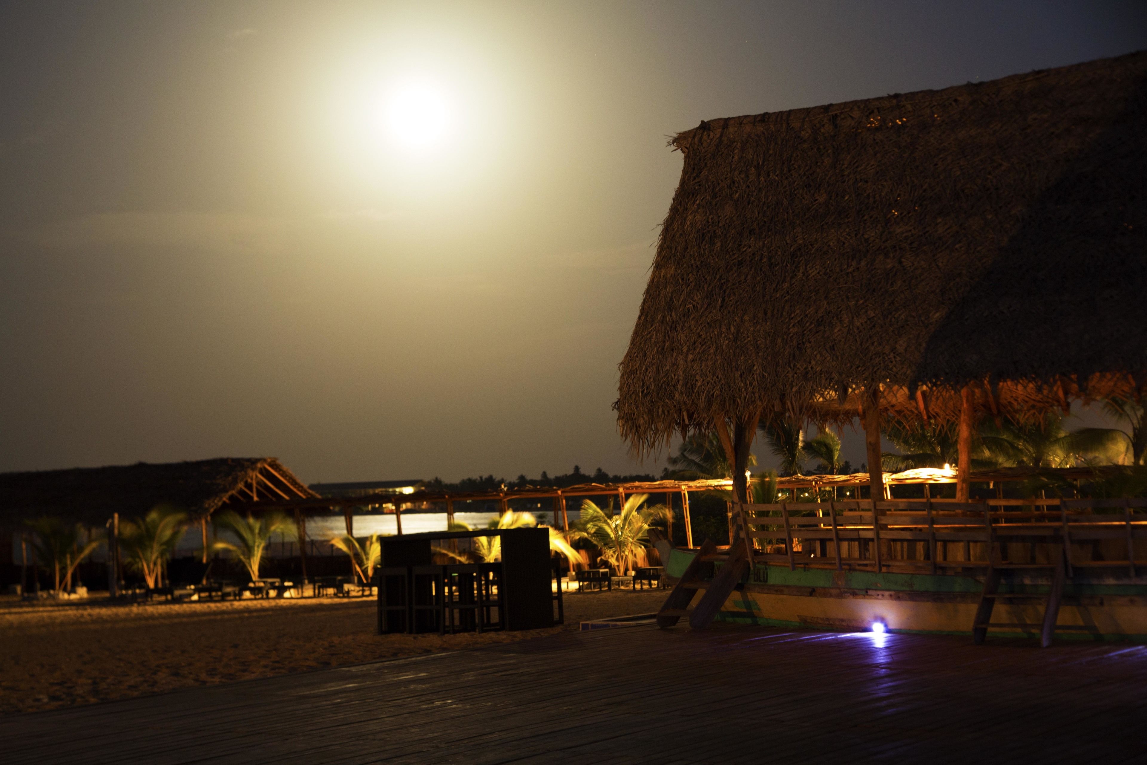 A beachside resort with a thatched-roof structure, wooden deck, and palm trees.