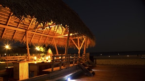 A wooden deck with a thatched-roof structure, likely a bar or dining area, overlooking a beach at night. - Maalu Maalu Resort & Spa (Pasikuda)