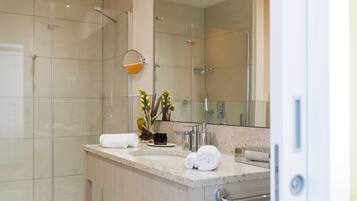Un baño moderno con cabina de ducha de vidrio, un espejo grande y encimera de granito.