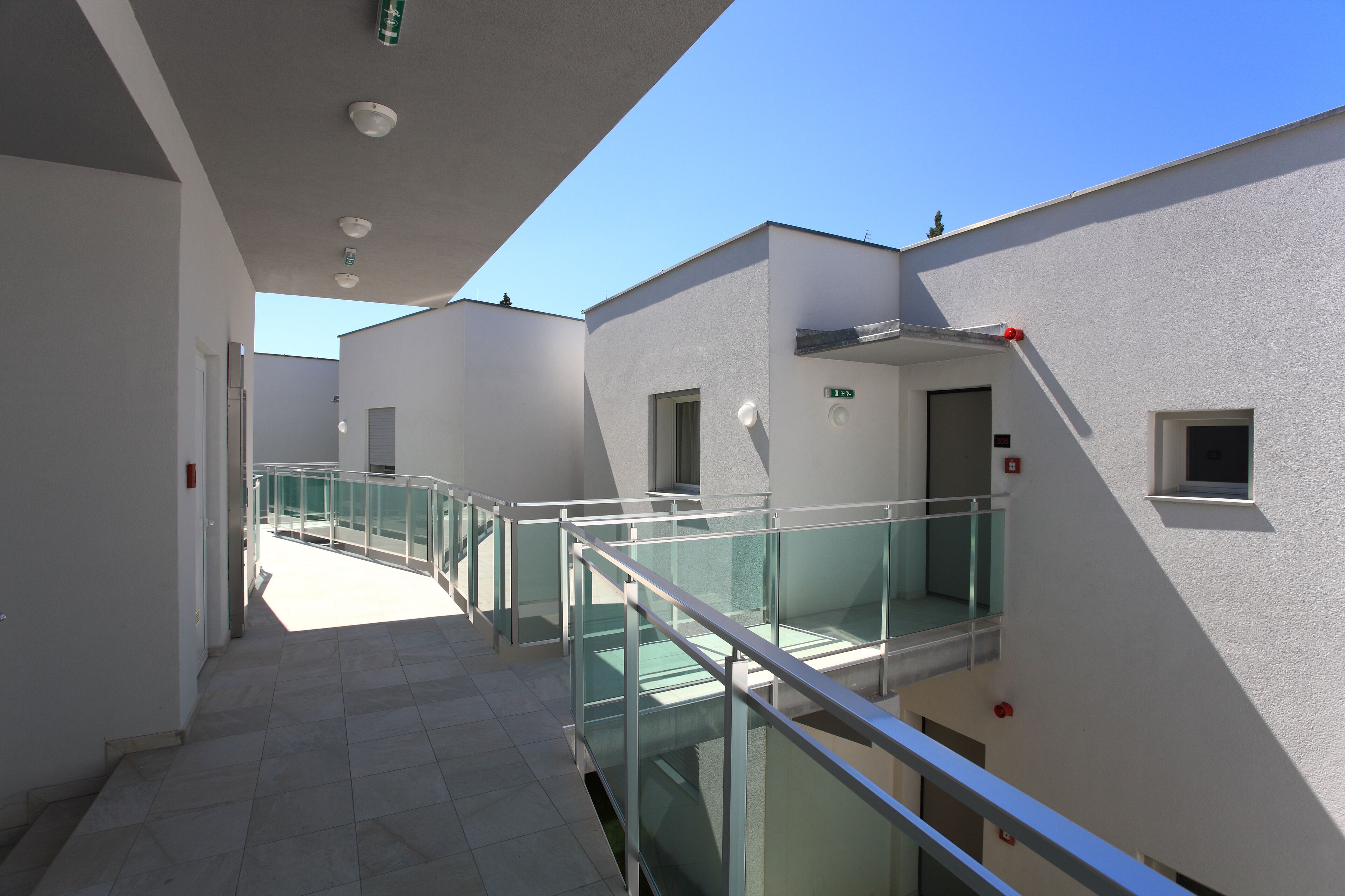 A modern building with a glass balcony, white walls, and a clear sky.