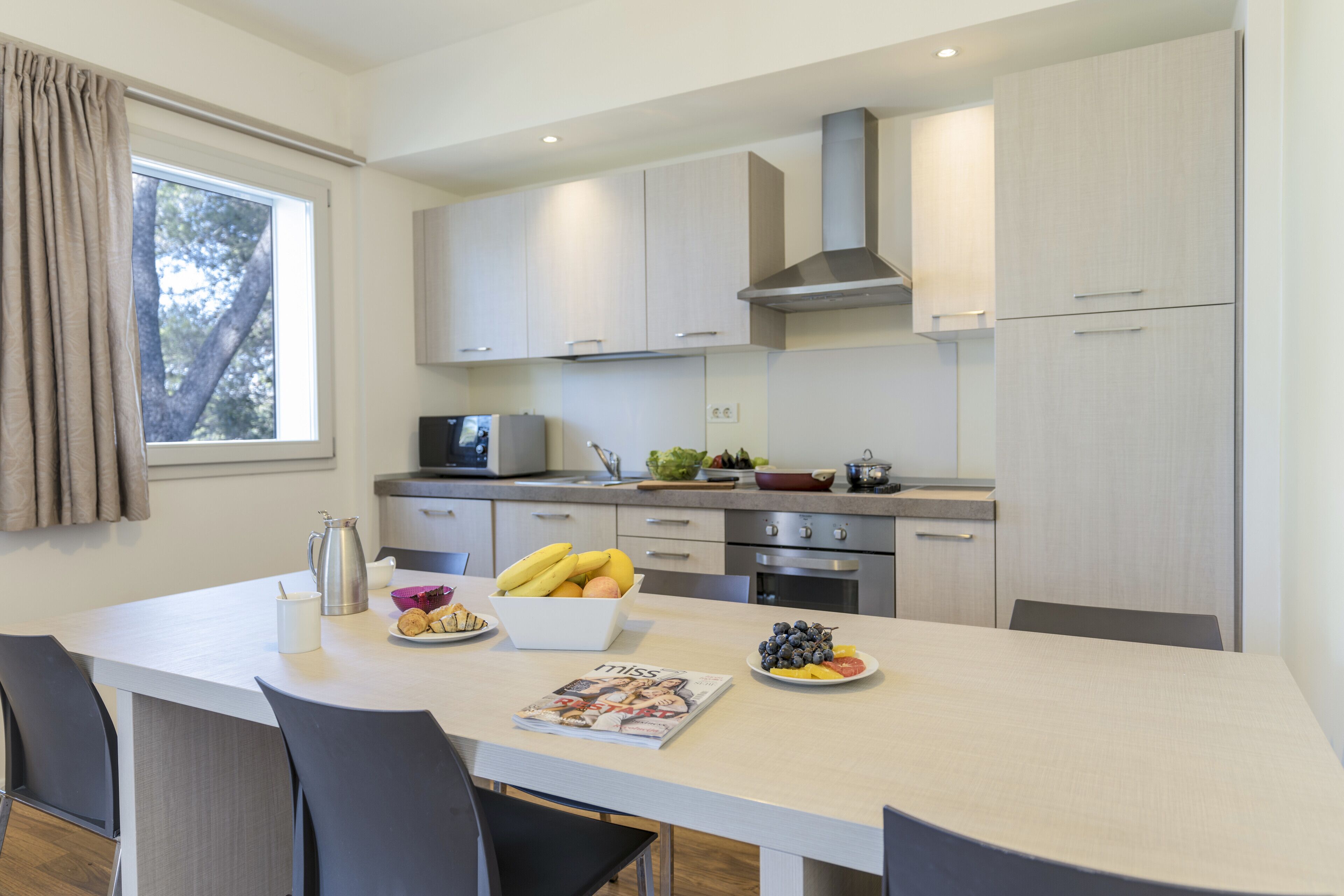 A modern kitchen with white cabinets, a stainless steel range hood, and a dining area with a white table and chairs.