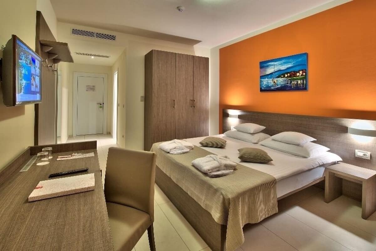 Habitación de hotel con cama, mesitas de noche, escritorio y televisor de pantalla plana, además de un cuadro en la pared.
