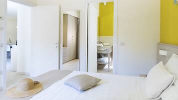 Una camera d'albergo con un letto, un cappello sul letto, un bagno con uno specchio e una parete gialla.