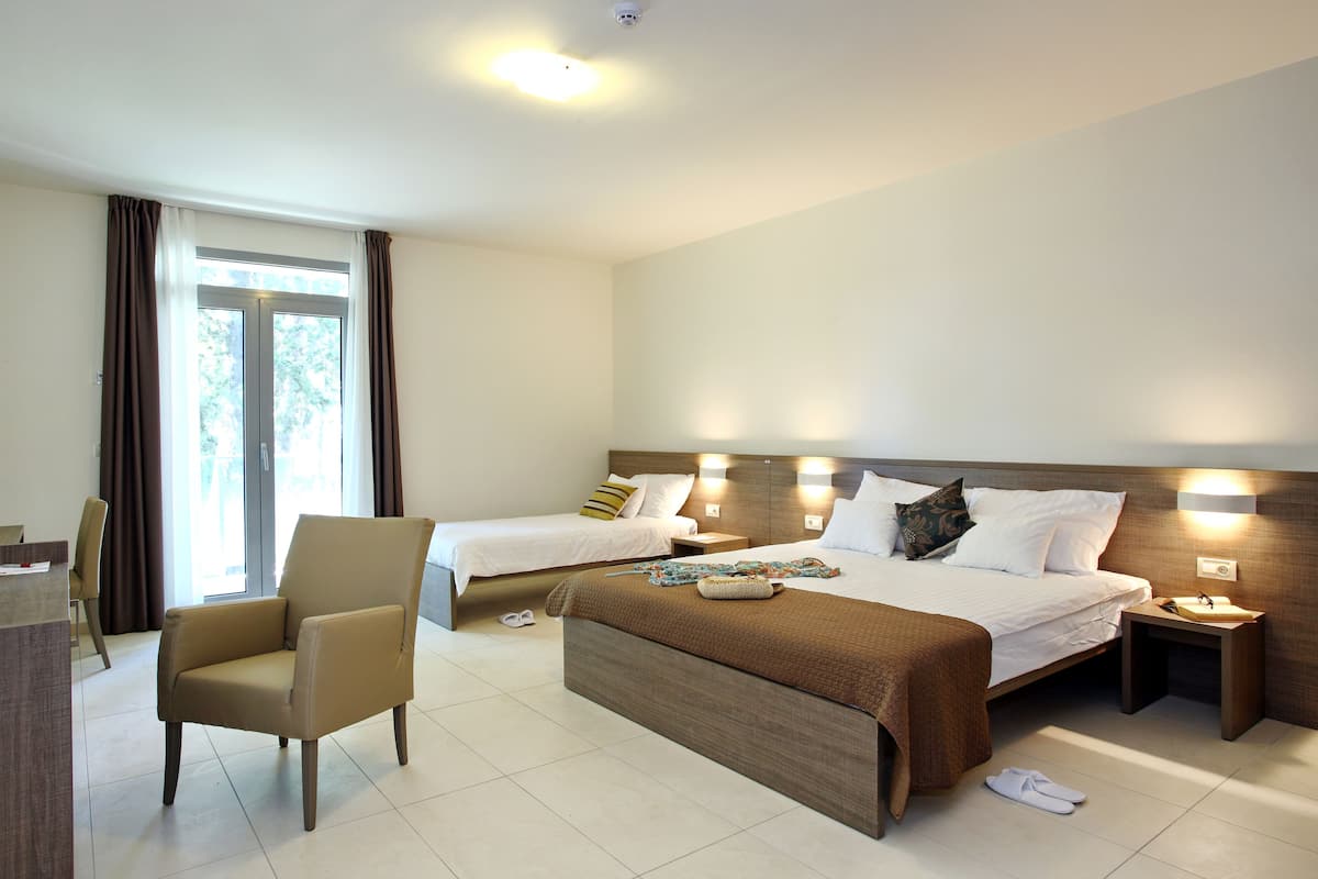 Una habitación de hotel con dos camas, una silla, un escritorio y una ventana con cortinas.
