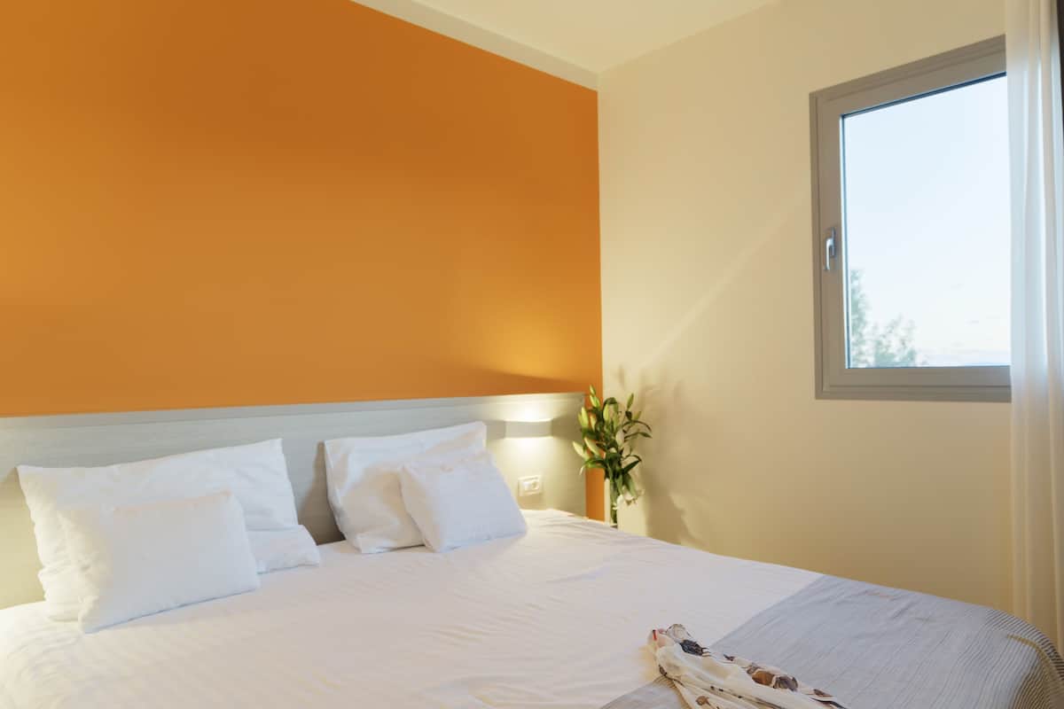 Una habitación de hotel con una cama grande, ropa de cama blanca y un ventanal con cortinas.