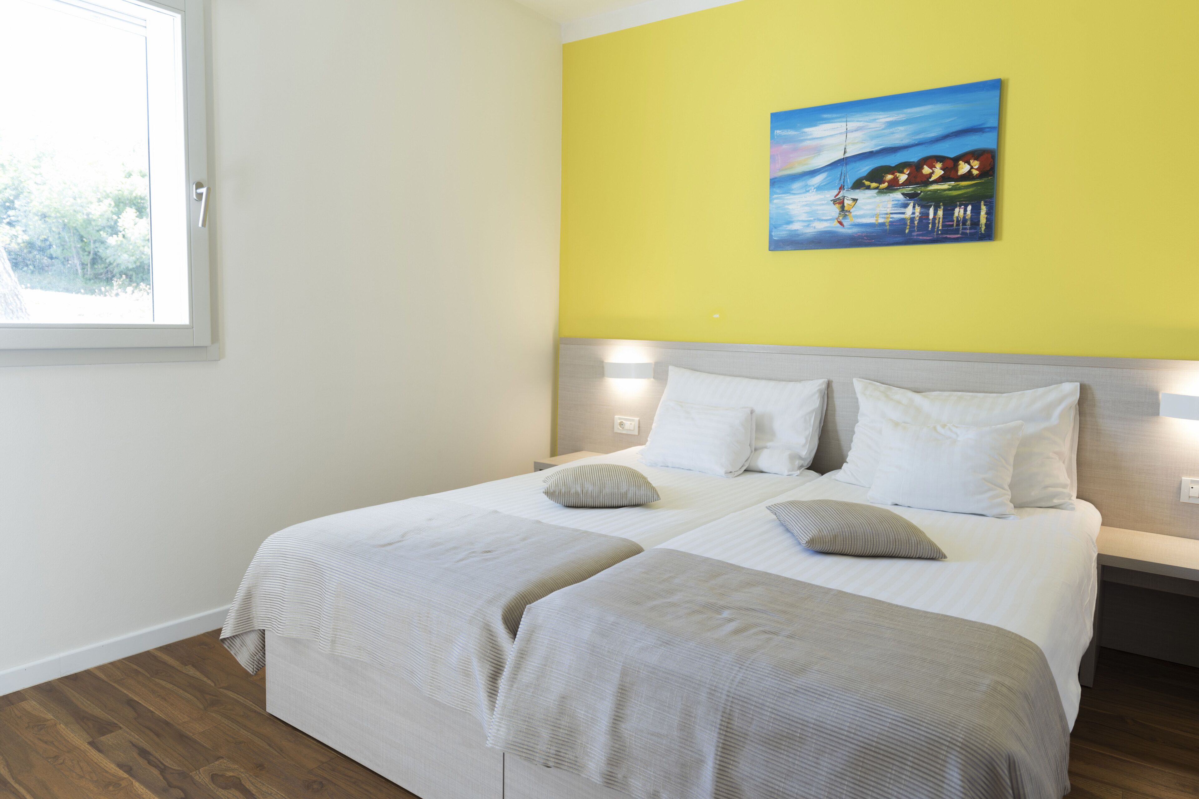 A double bed with two pillows, a bedside table, and a painting on the wall.