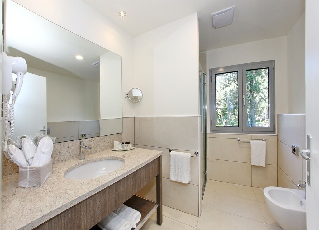 A modern bathroom with a large mirror, a sink, a shower, and a bidet.