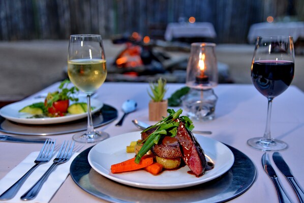 A dining table with plates of food, wine glasses, and cutlery.