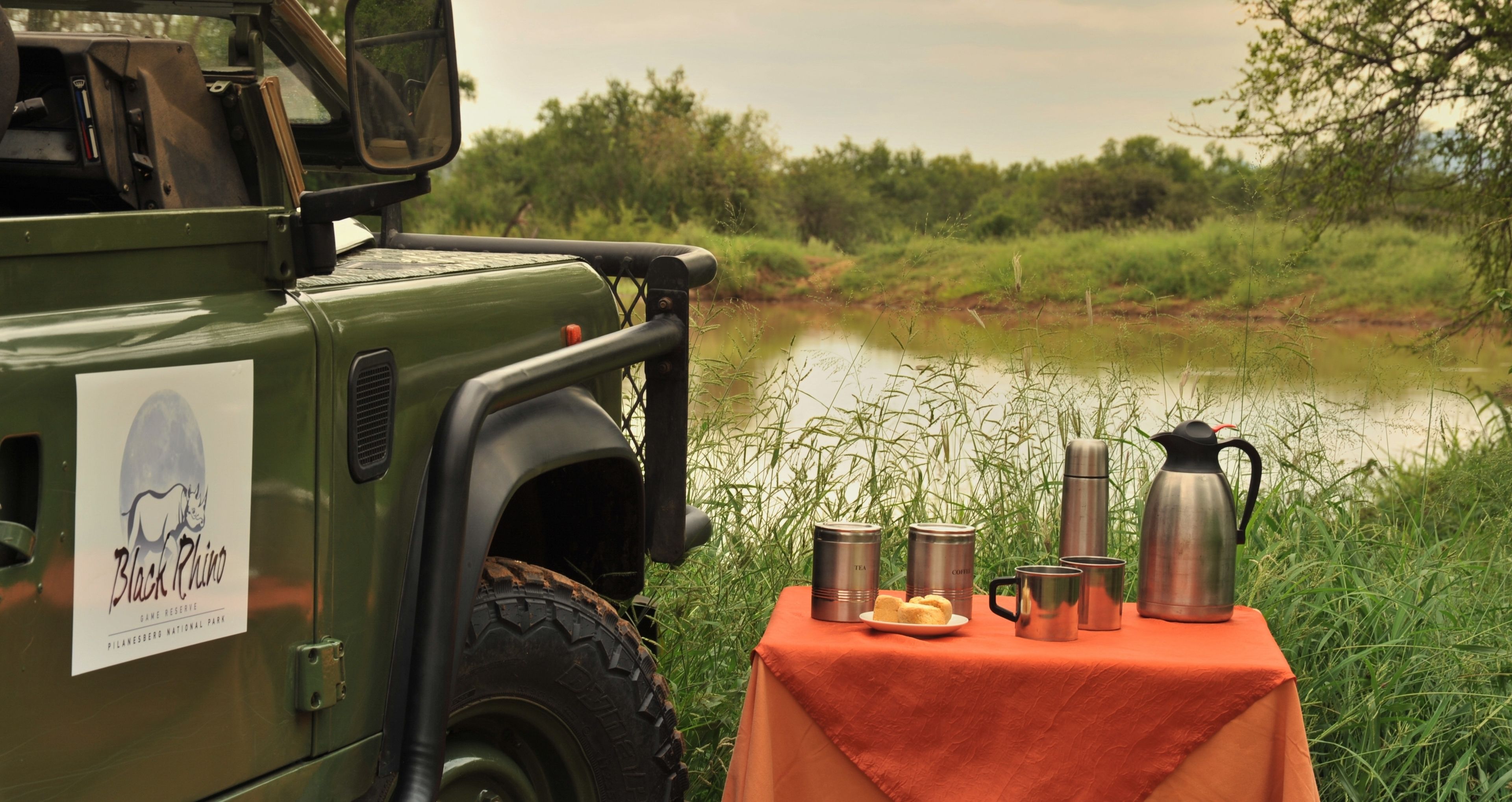 Un vehículo verde con una mesa instalada junto a un cuerpo de agua, mostrando un letrero de Black Rhino y varios contenedores de acero inoxidable.