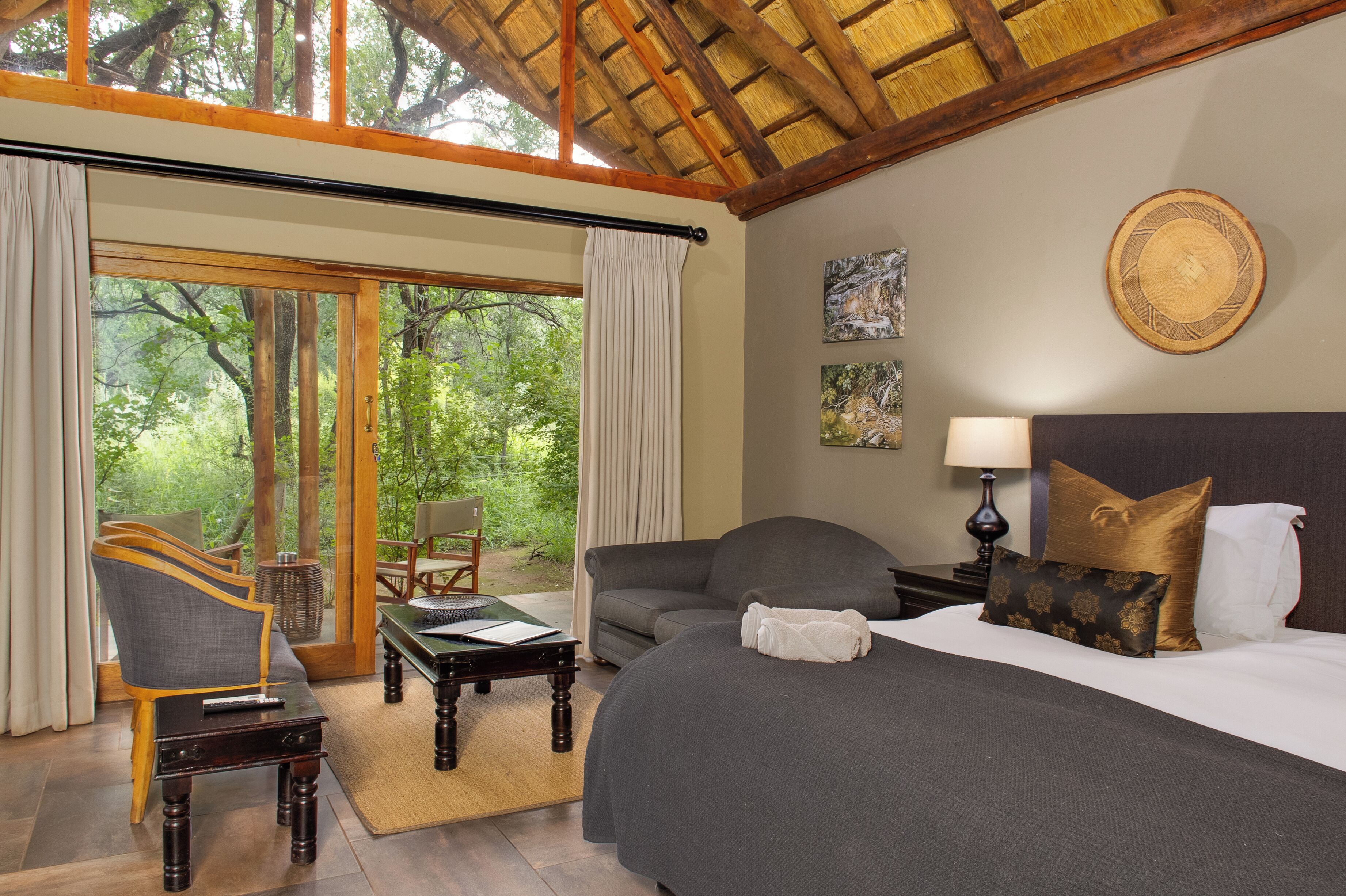A hotel room with a bed, a sofa, a chair, a table, and a view of the outdoors.