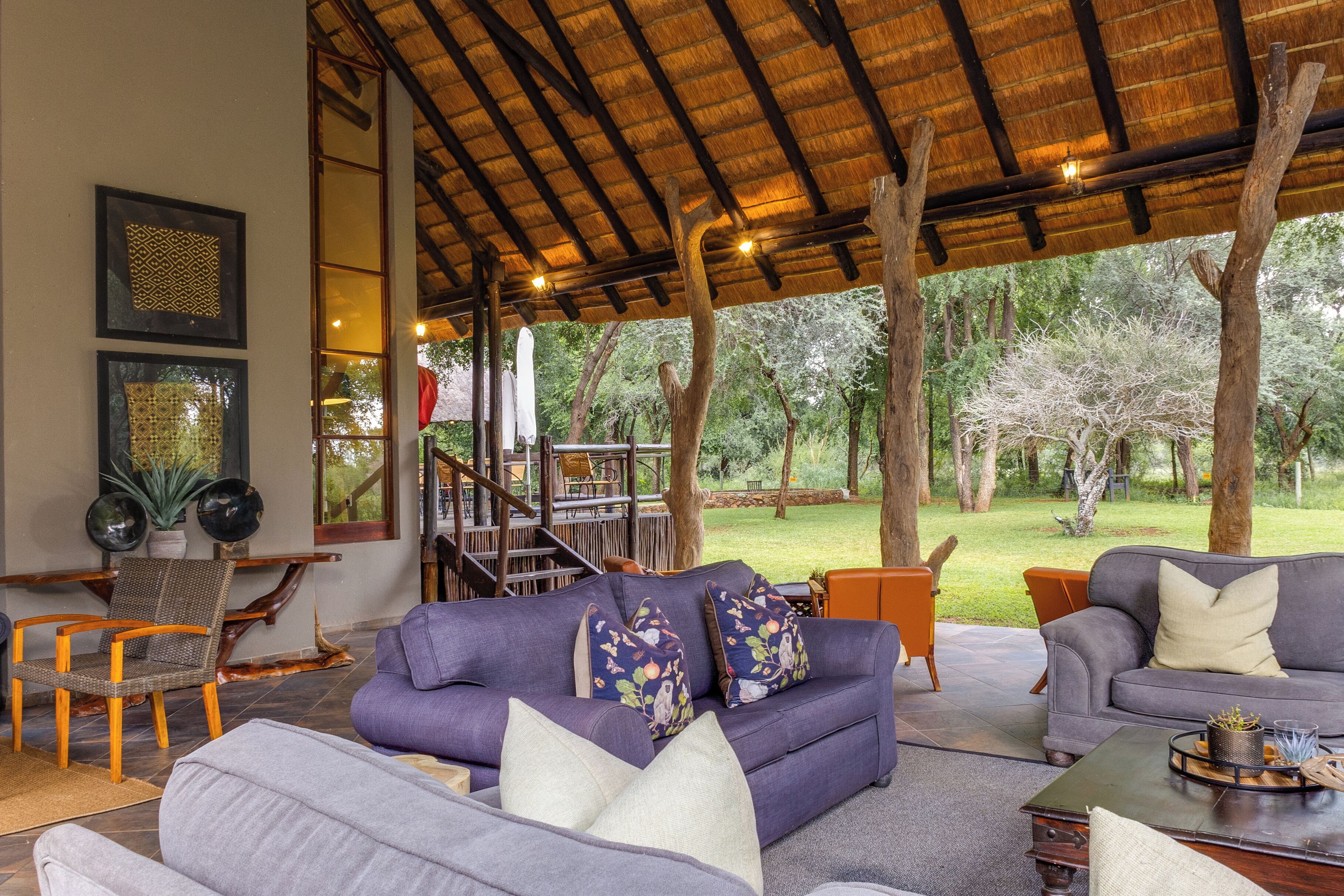 A covered outdoor seating area with a sofa and chairs, a staircase, and a view of the surrounding trees.