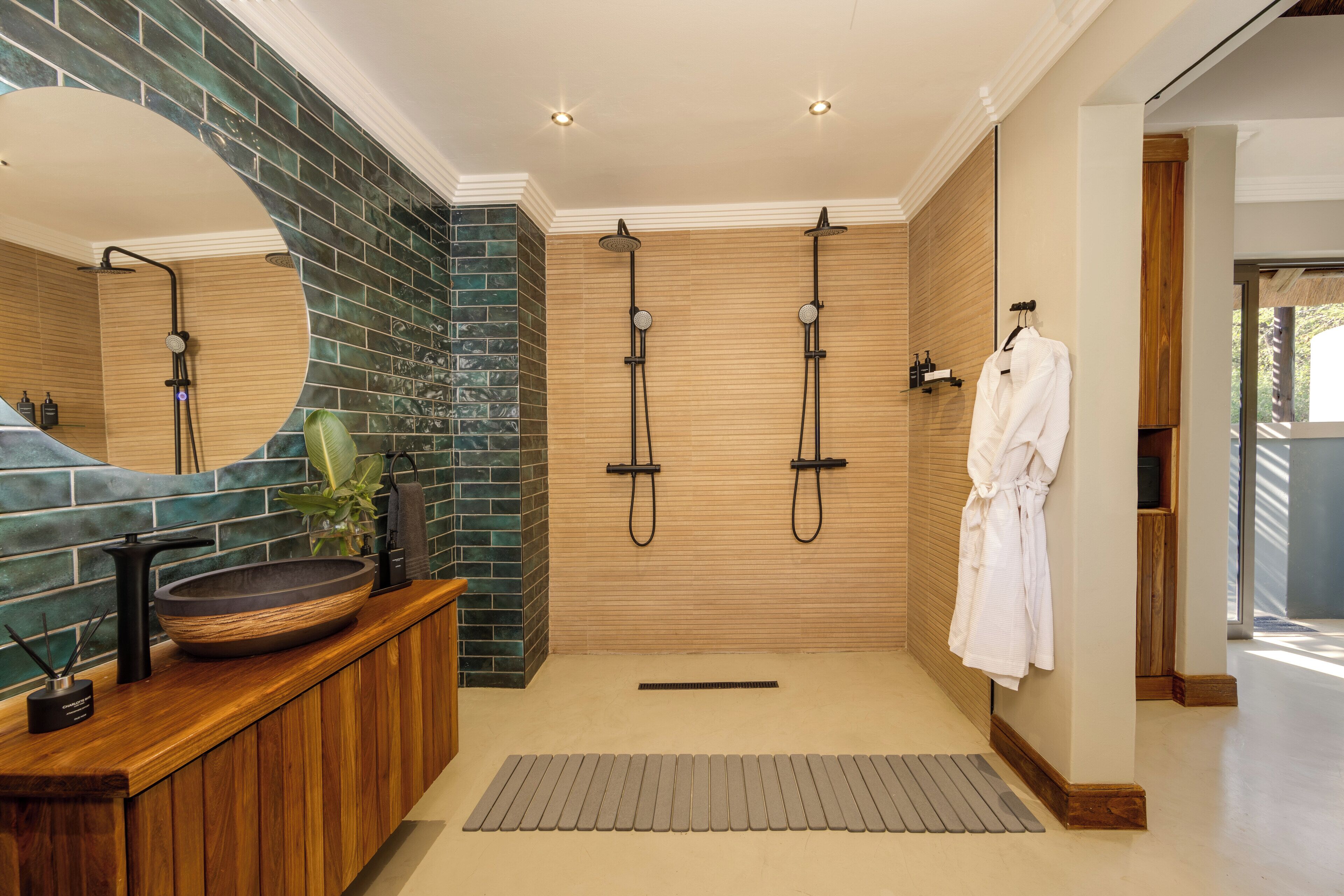 Un baño moderno con tocador de madera, un espejo grande, un lavabo redondo y una zona de ducha con dos cabezales.
