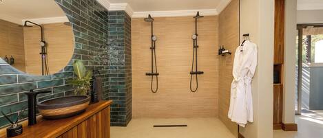 Un baño moderno con tocador de madera, un espejo grande, un lavabo redondo y una zona de ducha con dos cabezales.