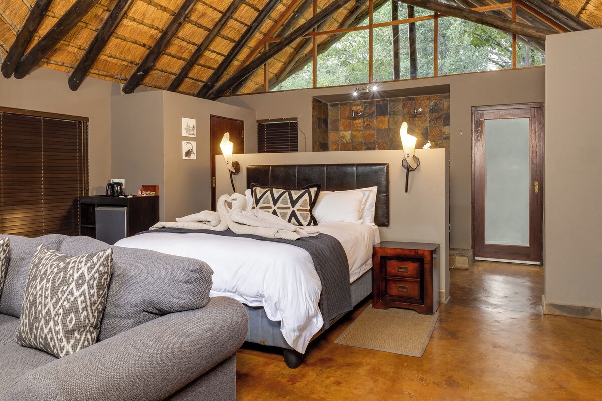 A bedroom with a large bed, a sofa, a nightstand, a wall-mounted light, and a door.
