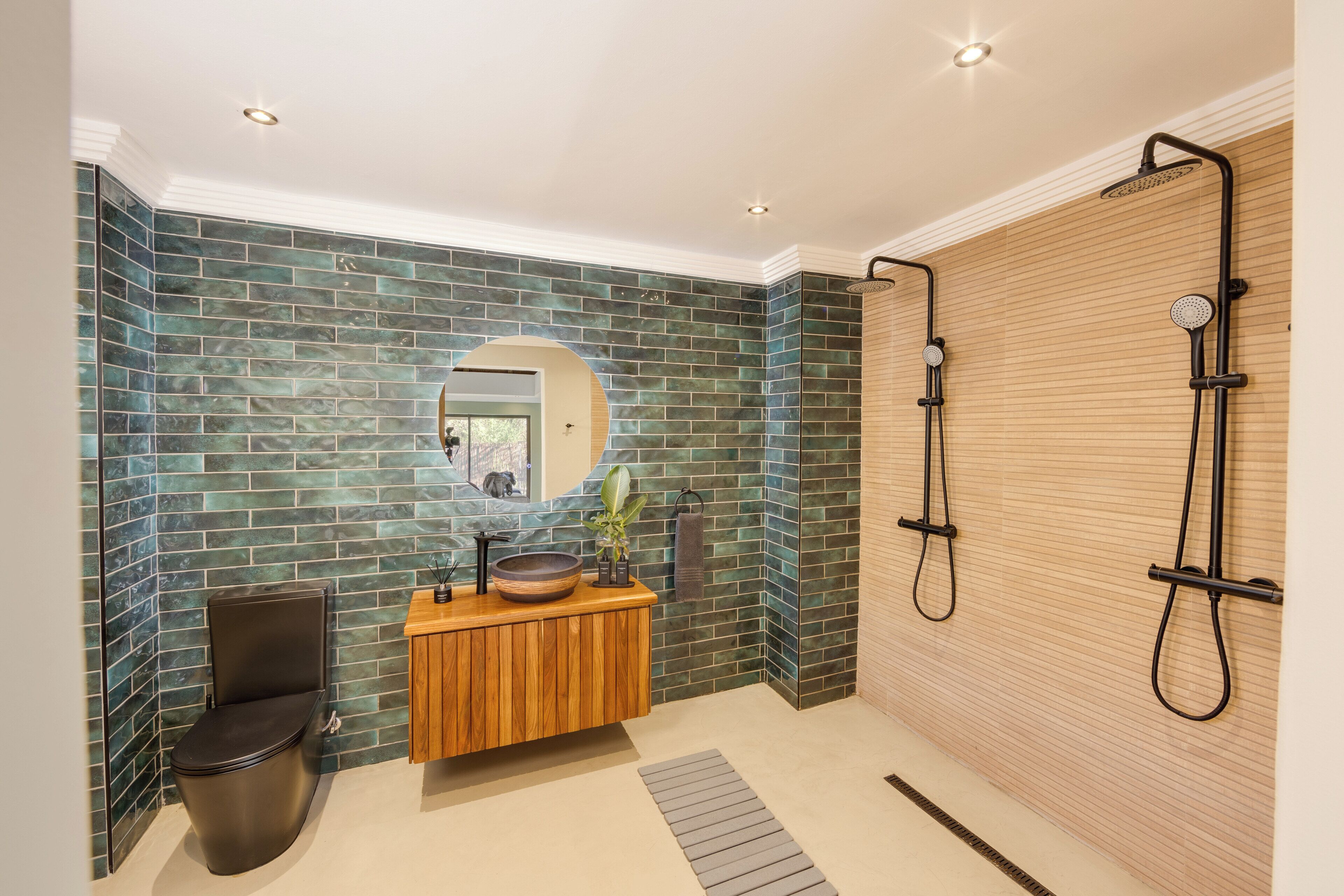 A modern bathroom with a wooden vanity, a round mirror, and a shower area with a wooden door.