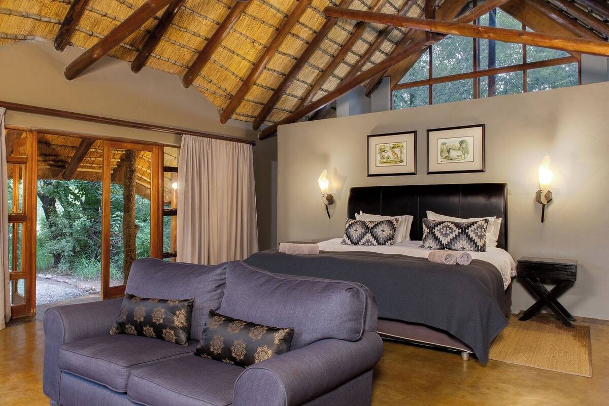 A bedroom with a large bed, a sofa, and a window with curtains.