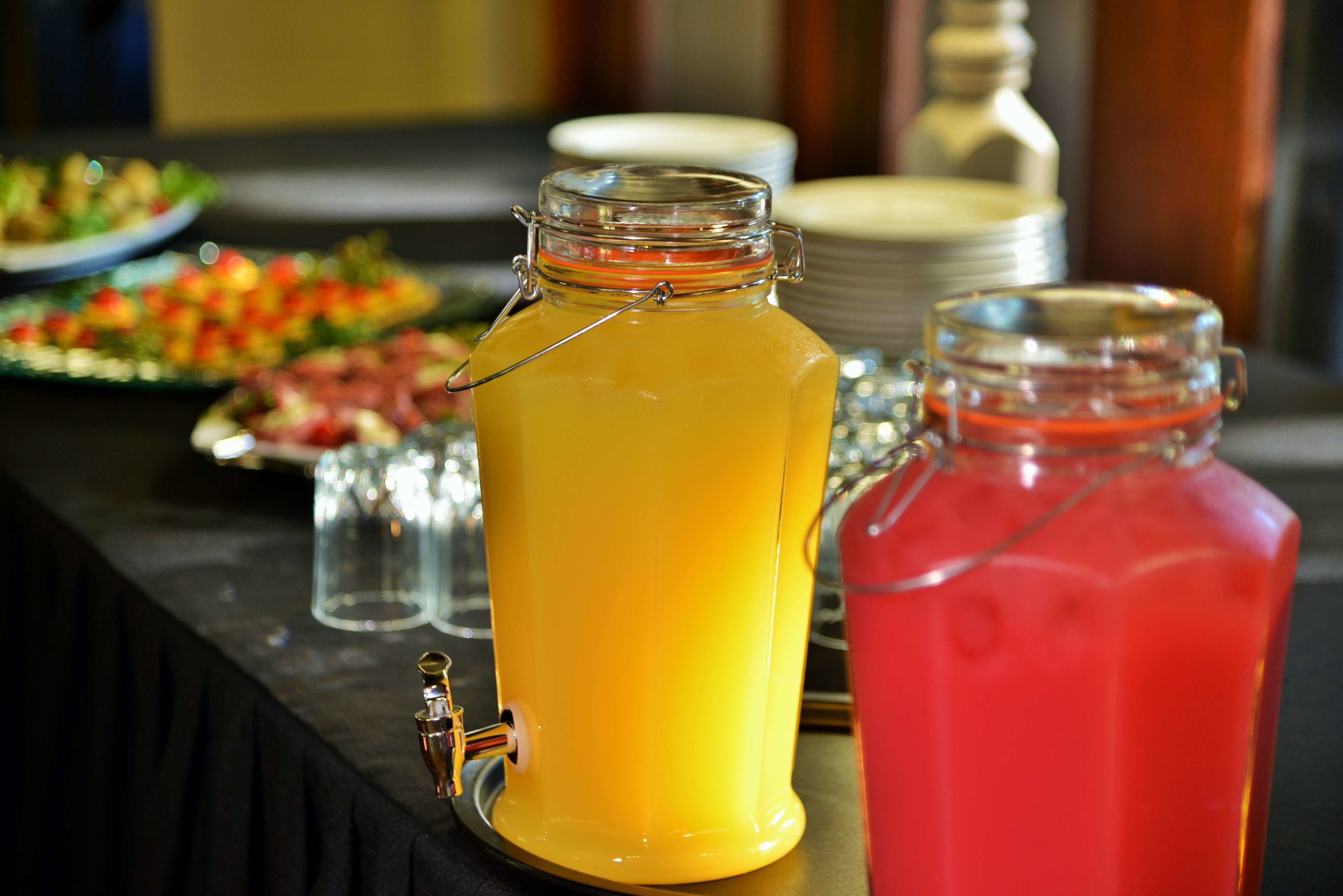 A beverage station with two glass jars, one containing a yellow drink and the other a red drink, with a tap on the yellow jar.