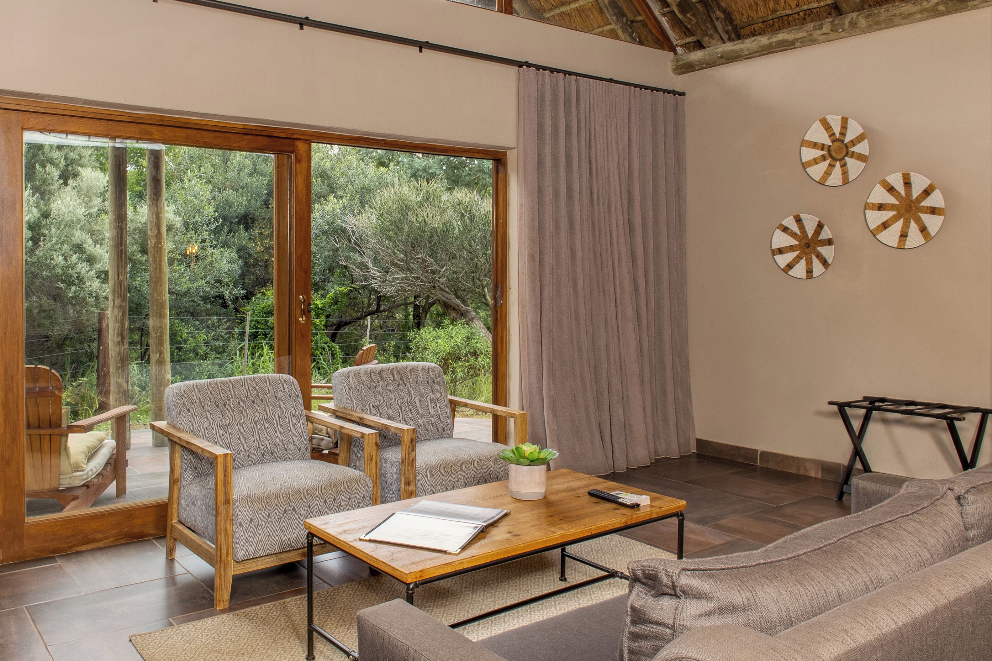 Una sala de estar moderna con un amplio ventanal corredera que da a un jardín, dos sillones, un sofá, una mesita de centro y decoración mural.