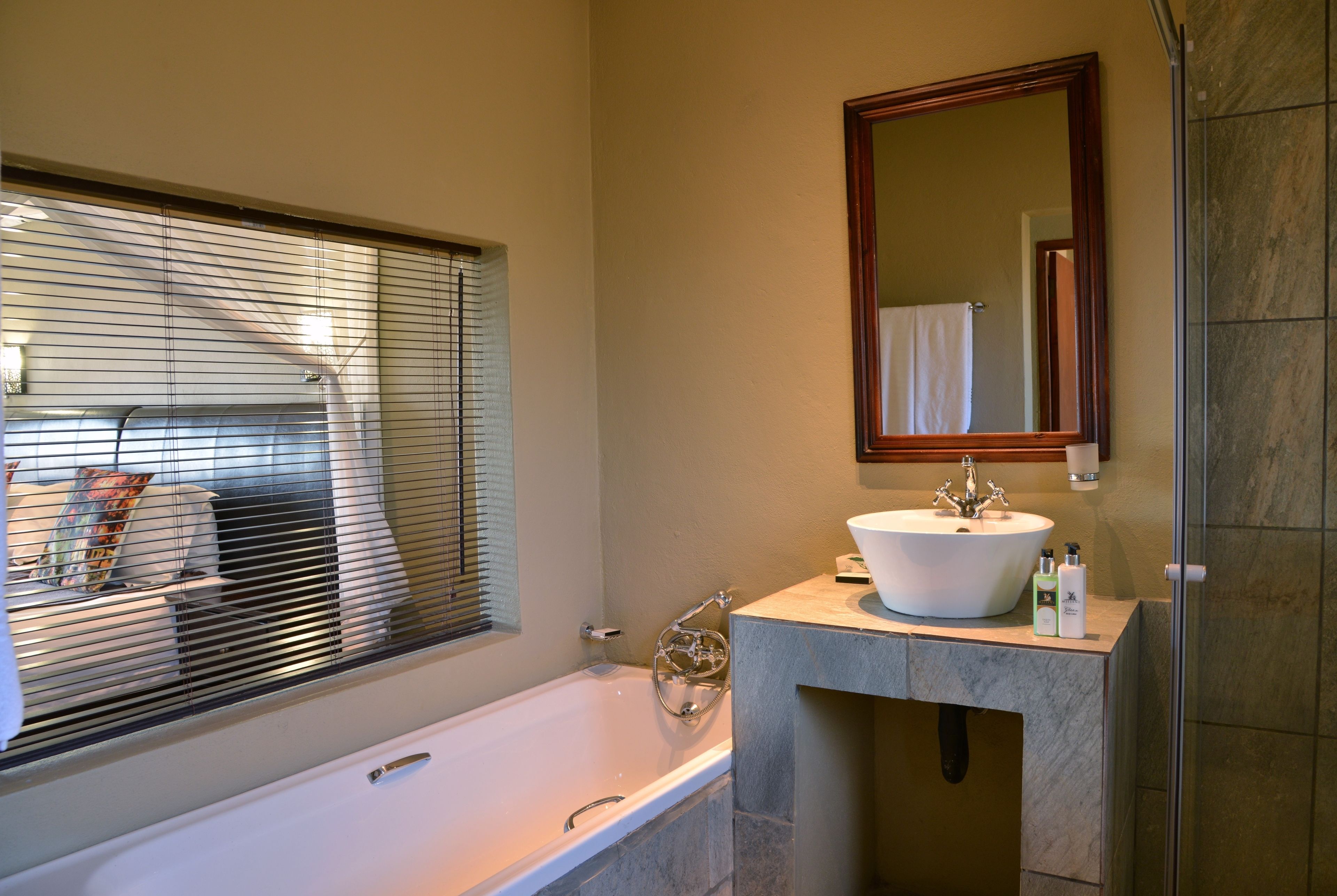 Un baño con bañera, lavamanos, espejo y ventana con persianas.