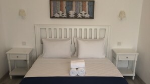 A large bed with white bedding, two pillows, and two rolled towels. There are two bedside tables, each with a lamp. A painting hangs above the bed. - Yasemin Alacati - Adult Only (Cesme)