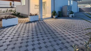 Un edificio moderno a due piani con tetto piano, un ingresso centrale e un cortile lastricato.