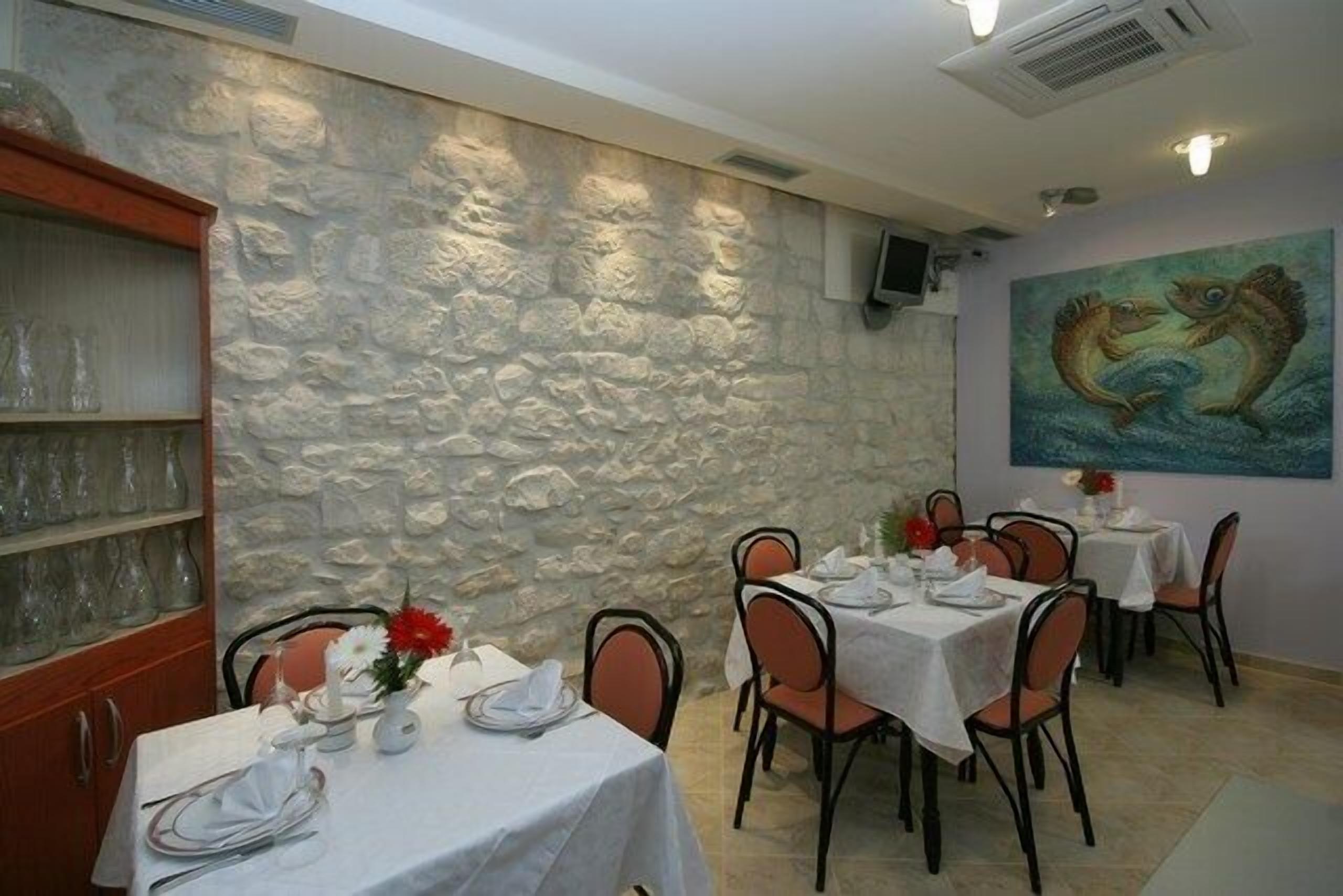 A restaurant with stone walls, white tablecloths, and orange chairs.