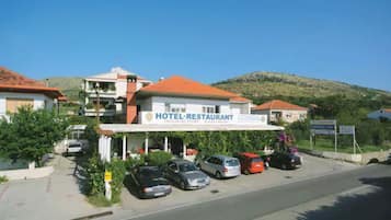 Un hotel con techo rojo, una cartelera y varios coches estacionados al frente.