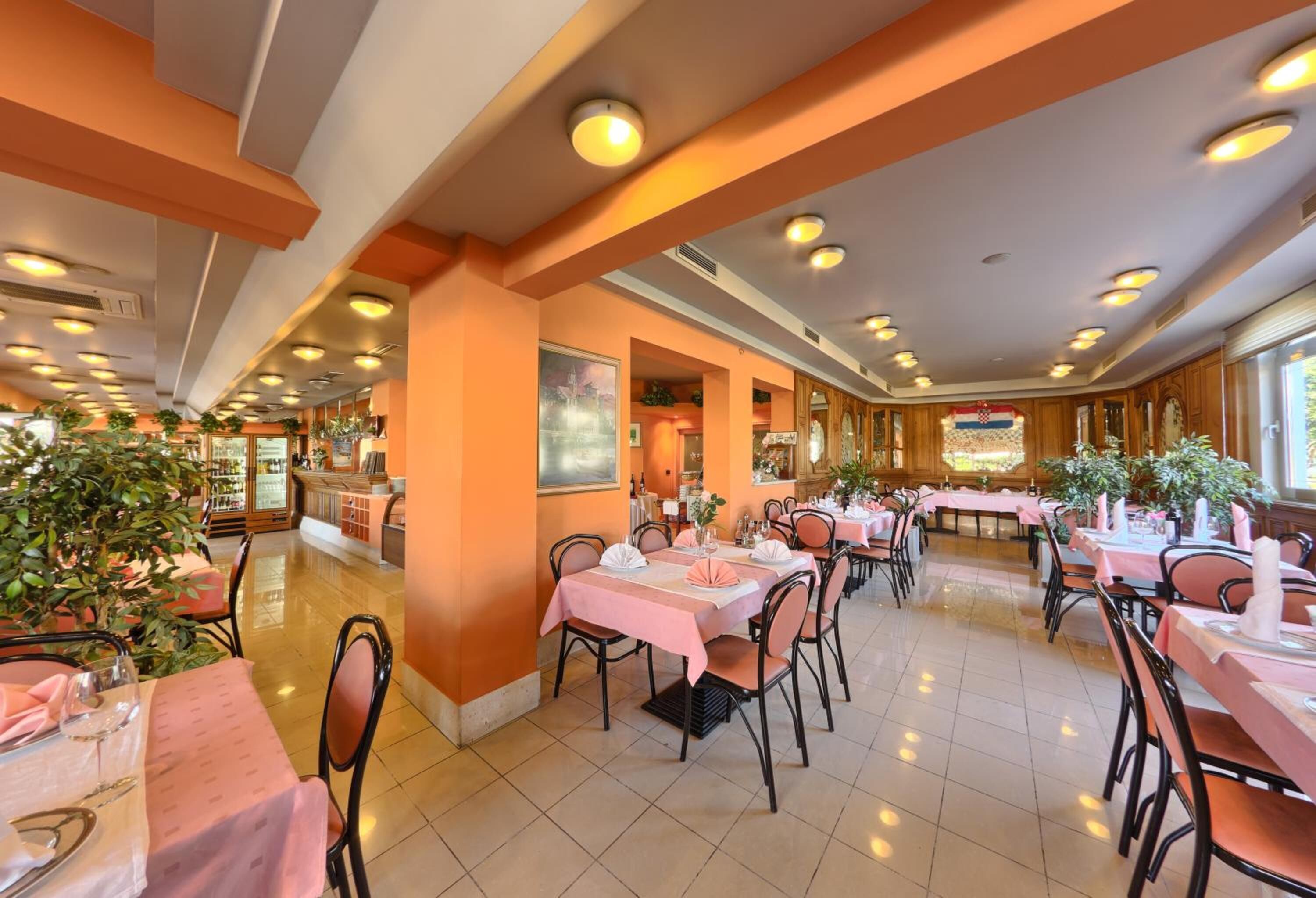 Un comedor espacioso con varias mesas y sillas, una columna central y luces de techo.