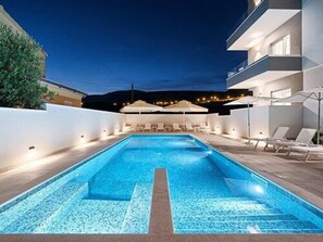 A rectangular swimming pool with a tiled deck, surrounded by lounge chairs and umbrellas, indicating a resort setting. - Hotel Trogirski Dvori (Trogir)