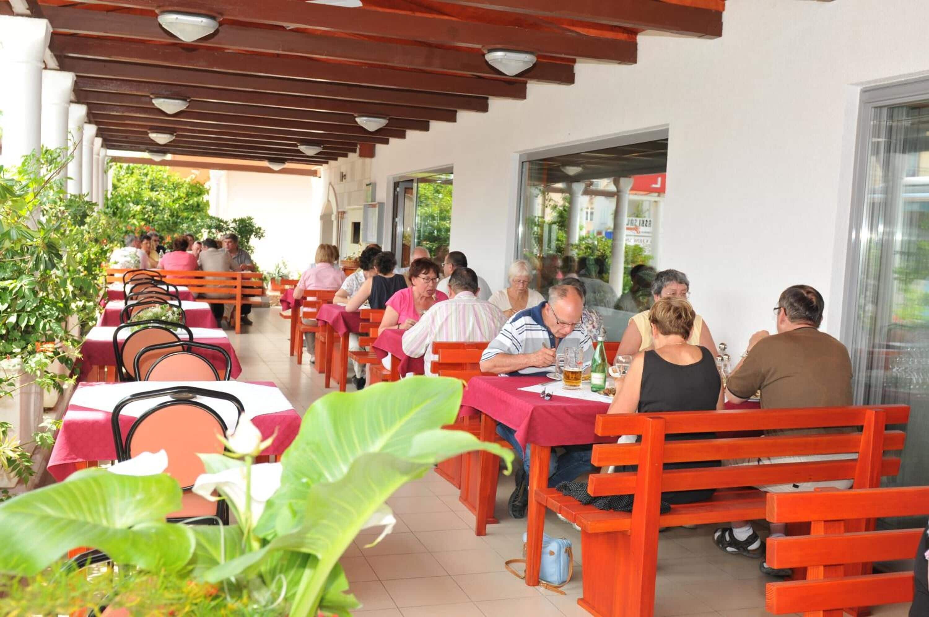 An outdoor dining area with wooden benches and tables, surrounded by potted plants.