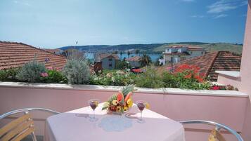 A table with a fruit bowl and two glasses of red wine, overlooking a coastal village with terracotta-roofed houses.