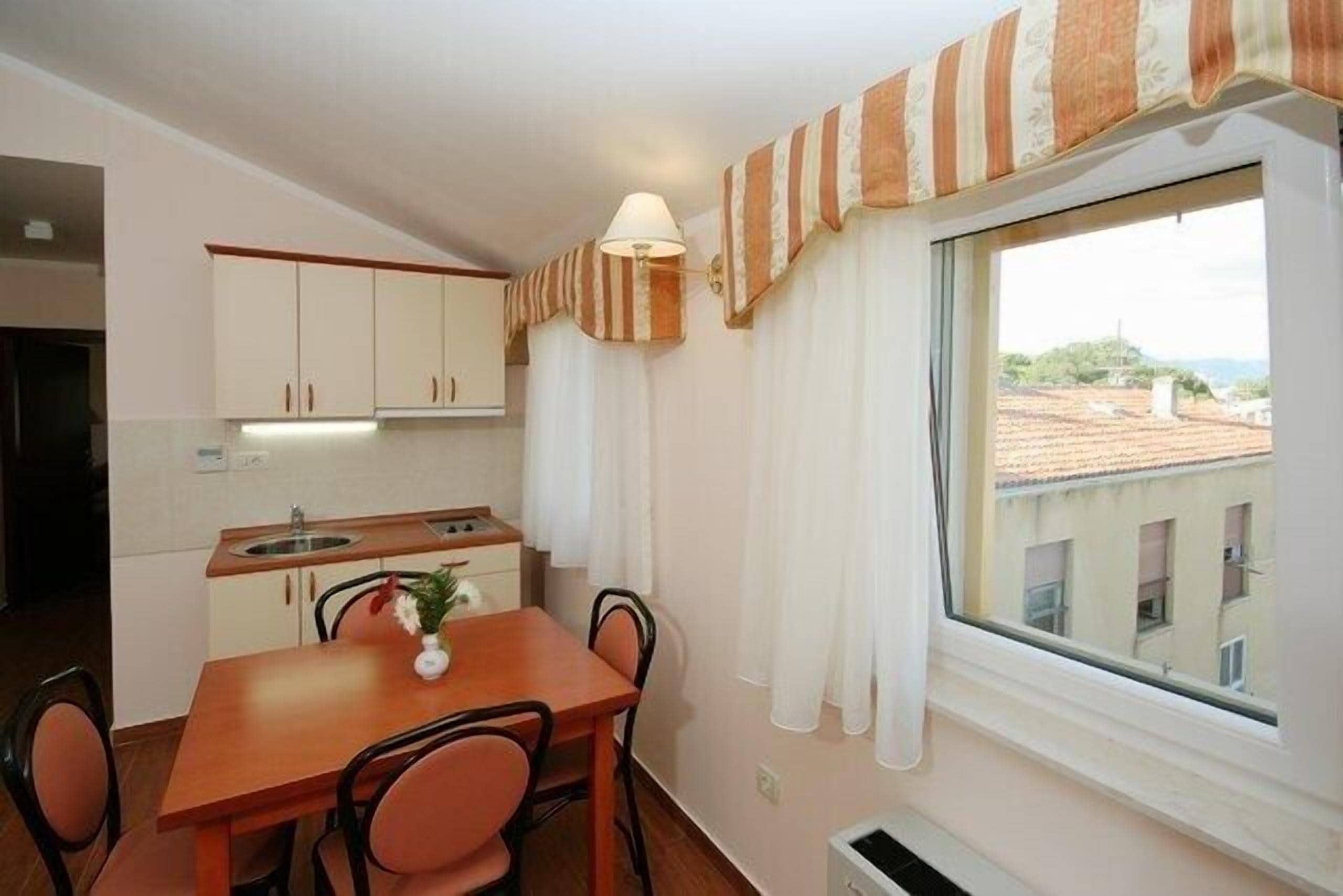 A compact kitchen with a dining table and chairs, a window with curtains, and a view of buildings outside.