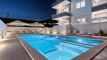 A modern hotel with a swimming pool, lounge chairs, and umbrellas.