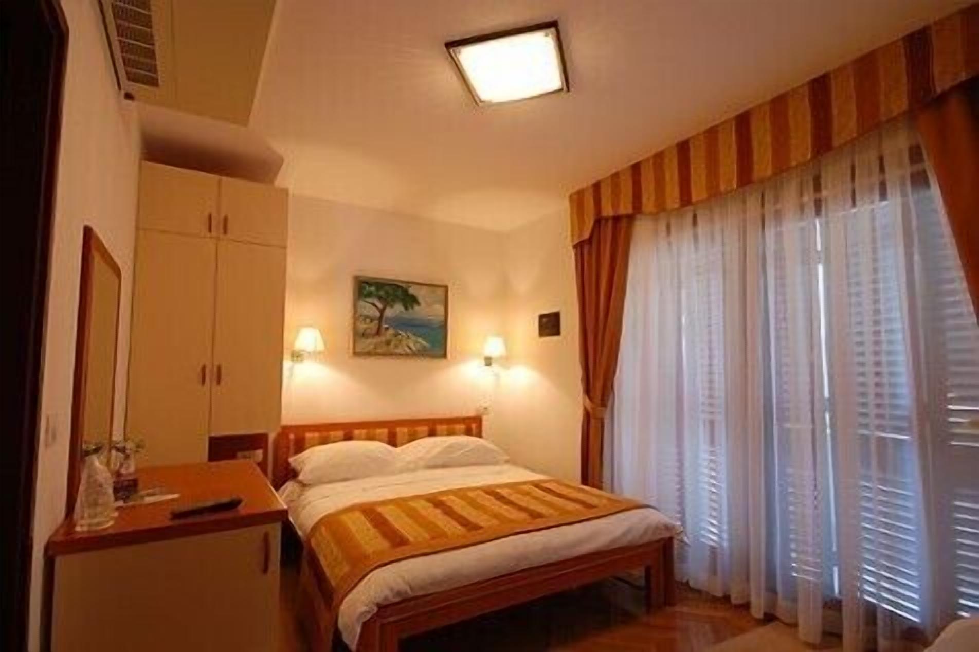 A bedroom with a bed, a nightstand, a painting on the wall, and a window with curtains.