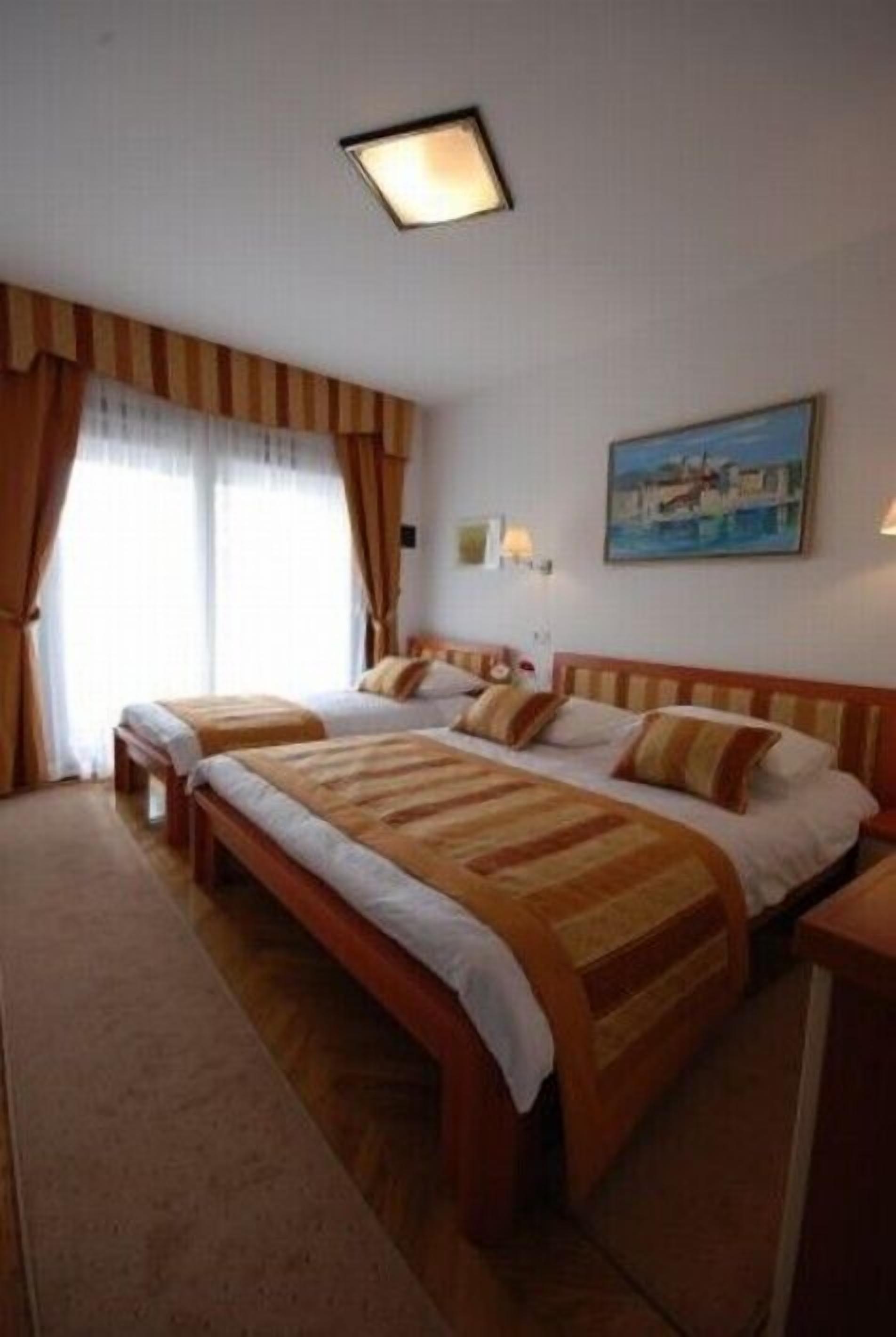 A hotel room with two beds, a painting on the wall, and a window with curtains.