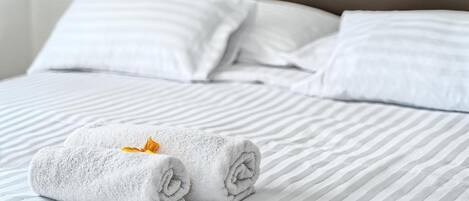 A neatly made bed with striped bedding and two rolled towels with a flower.