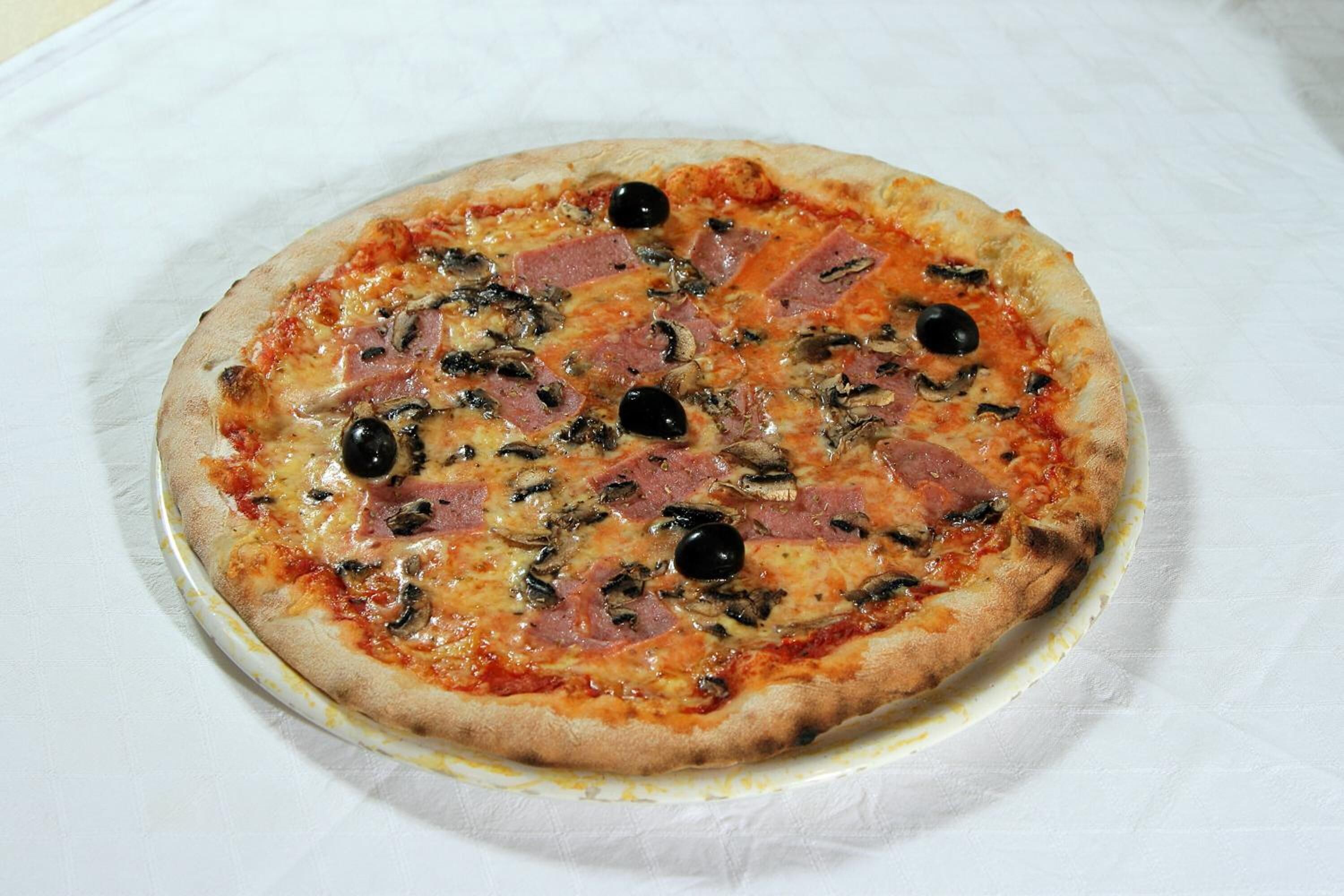 Pizza met ham, olijven en champignons op een wit bord.