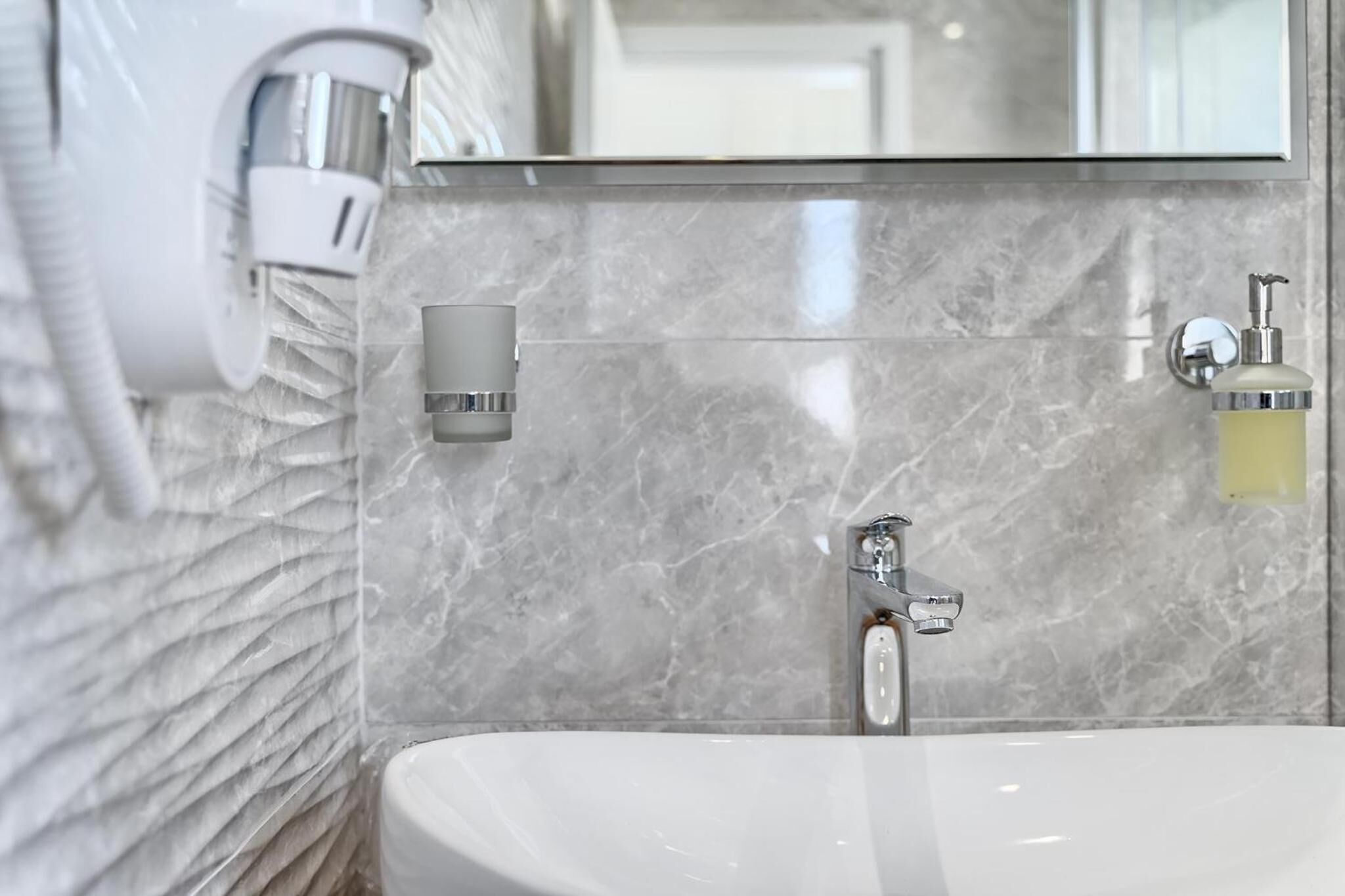 Un baño moderno con salpicadero de mármol, lavabo blanco, cabezal de ducha de mano y dispensador de jabón.