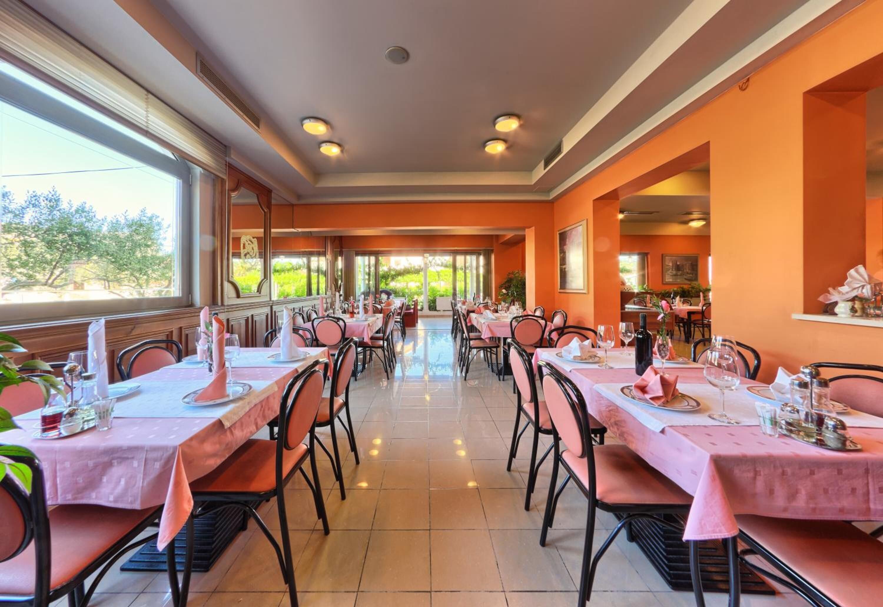 A dining area with tables set for multiple guests, large windows, and a view of greenery outside.