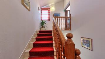 Una escalera con peldaños alfombrados de rojo, barandillas de madera y cuadros en las paredes.