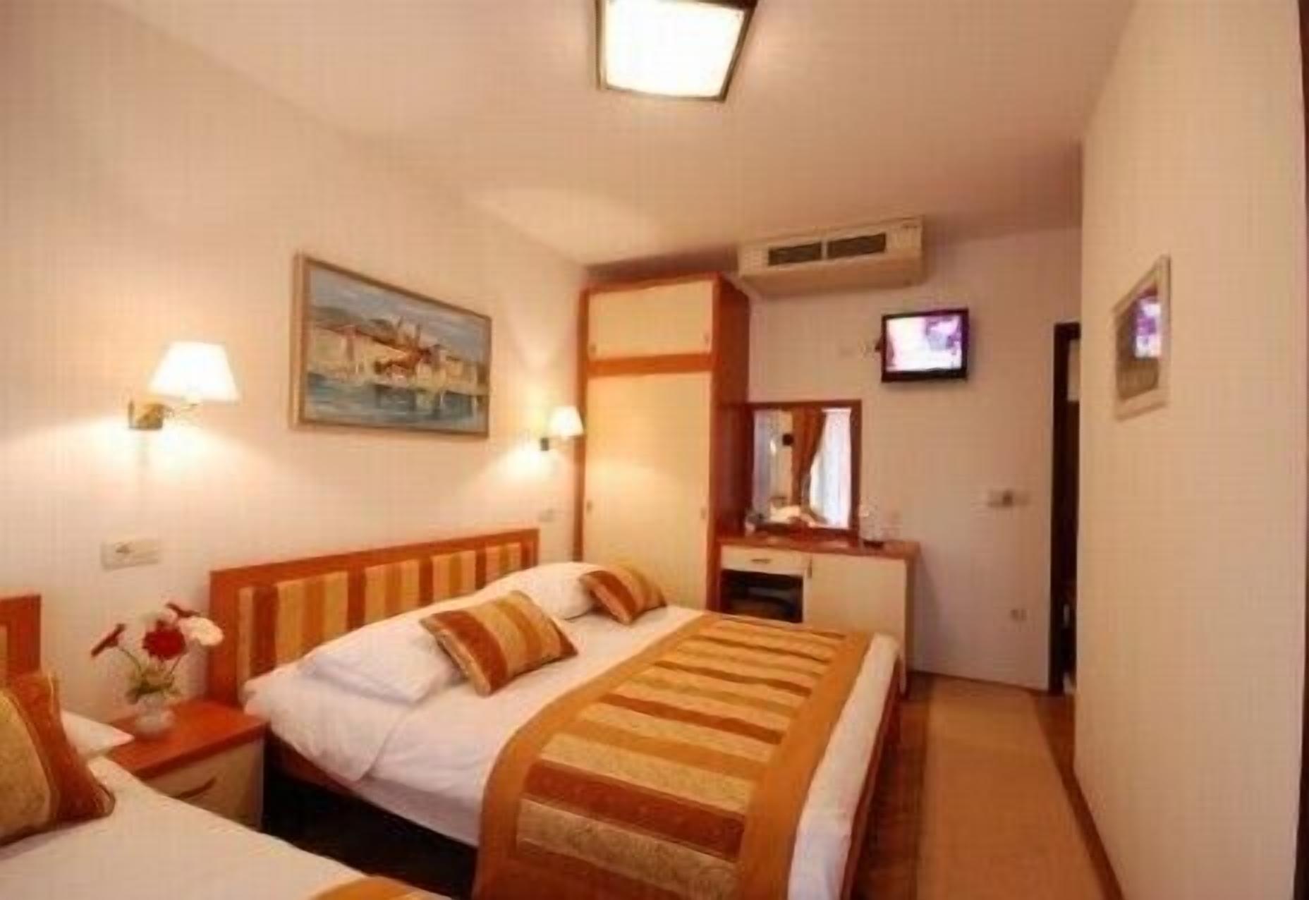 A hotel room with a bed, bedside tables, a TV, and a painting on the wall.