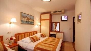 Habitación de hotel con cama, mesitas de noche, televisor y un cuadro en la pared.